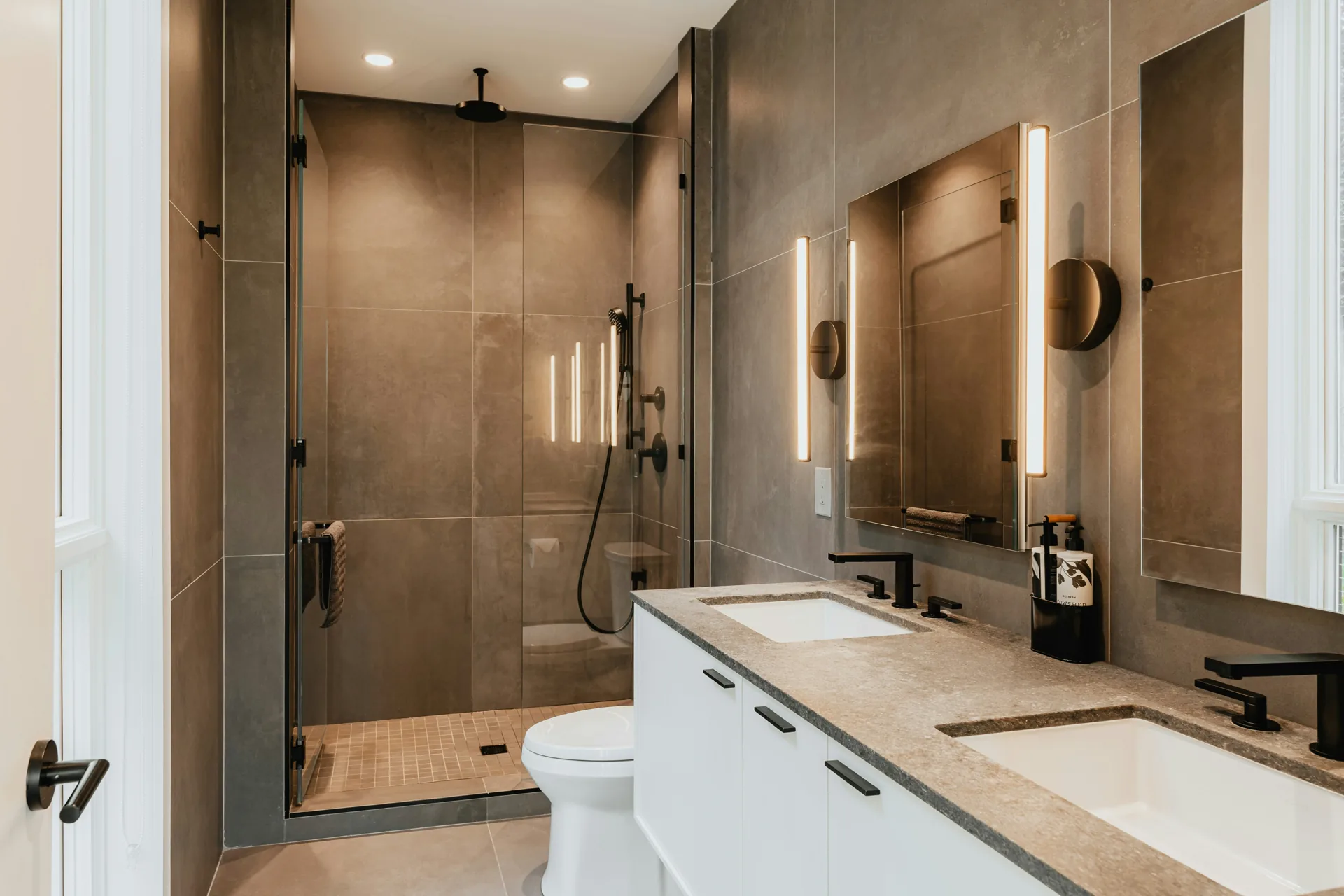 Modern bathroom with warm taupe tile, white vanity, and matte black hardware remodeled by Serden Group