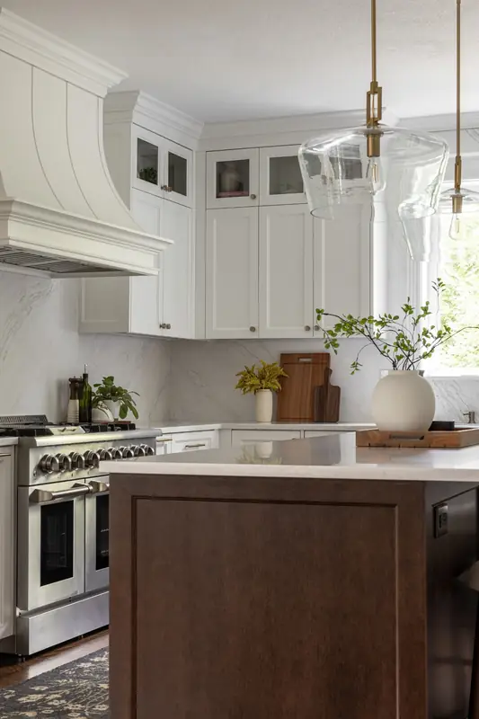 Custom painted range hood over a stainless dual-fuel range, with a full-height marble-look backsplash and glass-front uppers