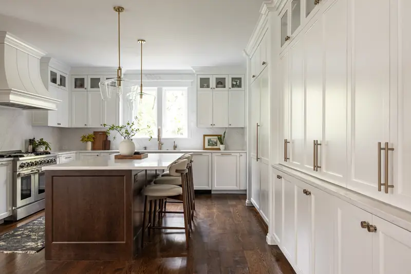 Long view along the floor-to-ceiling pantry wall toward the stained wood island and white shaker cabinetry