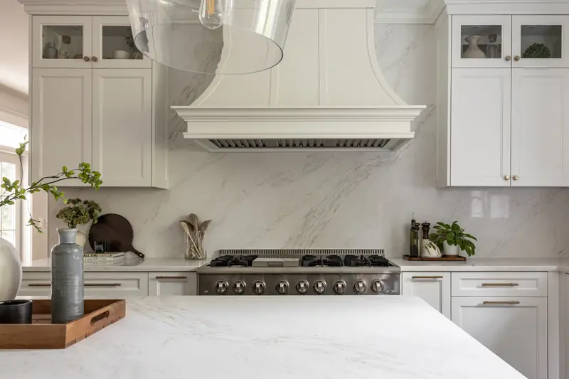 Painted range hood and full-height marble-look slab backsplash over a stainless range