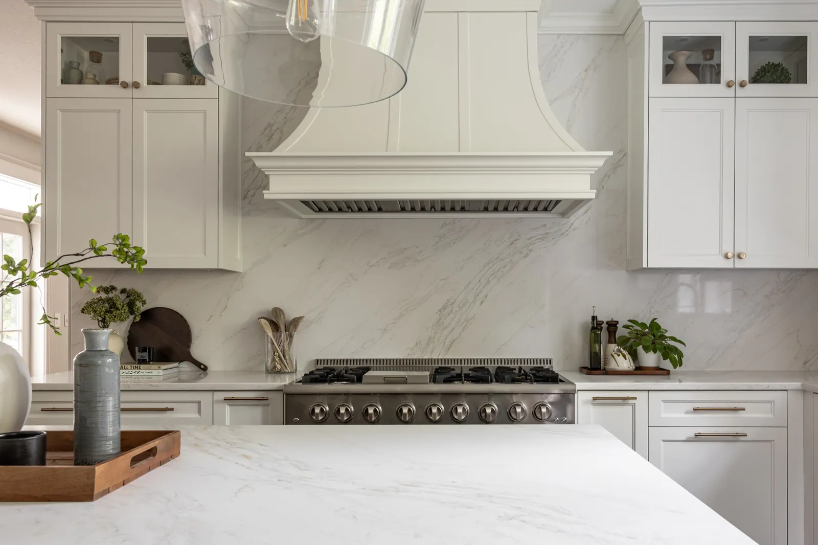 The new pro-style dual-fuel range under a custom curved hood, with a full-height quartz slab backsplash cut around it