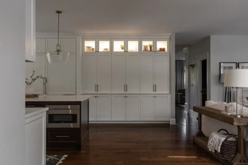 Wide view of the built-in cabinet wall with lit glass-front uppers and the hallway beyond
