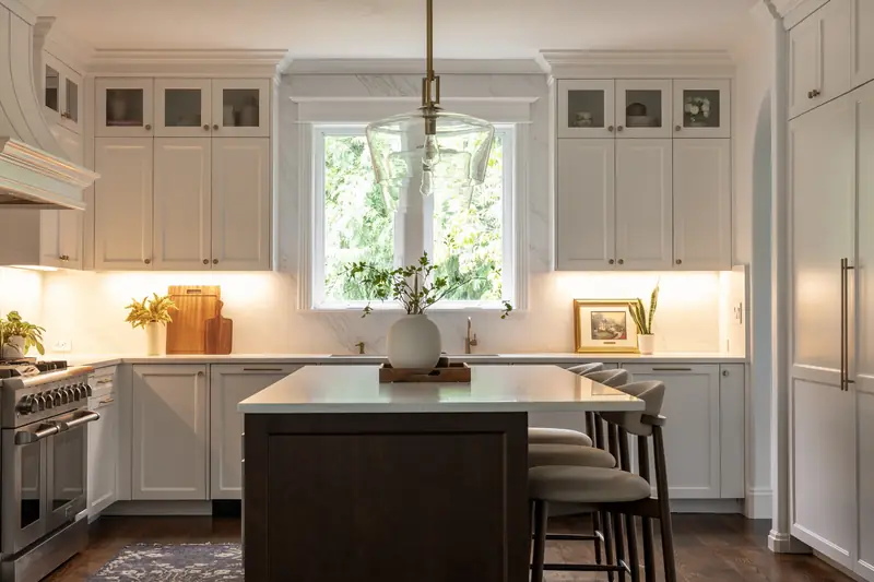 Kitchen window wall at dusk with warm under-cabinet lighting above the stained wood island