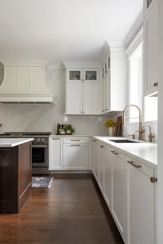White shaker sink run with a brass faucet leading toward the painted range hood