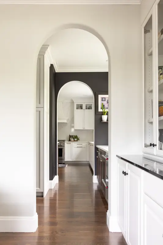 Arched doorway leading from the kitchen down a hallway with dark hardwood floors