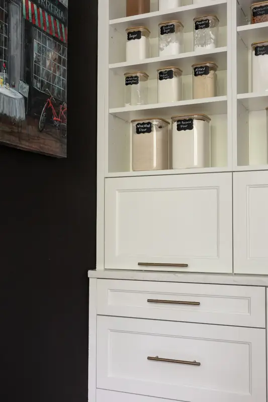Close view of pantry shelving with glass canisters above a white appliance garage