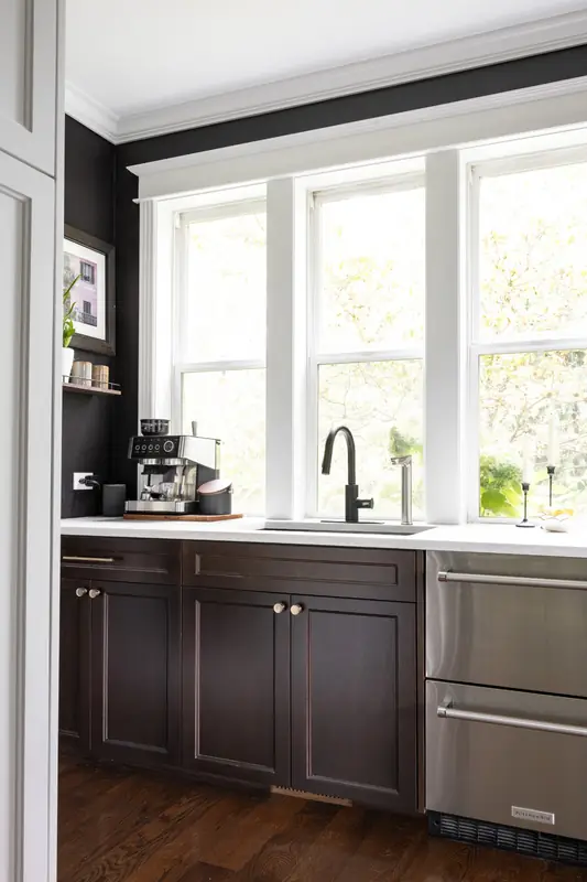 Butler's pantry with dark stained cabinets and stainless drawers beneath a triple window