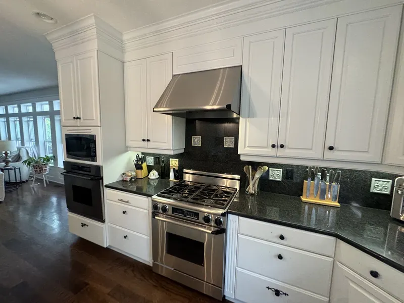 Before the remodel: the original range under an undersized stainless hood, with black granite and a dark tile backsplash