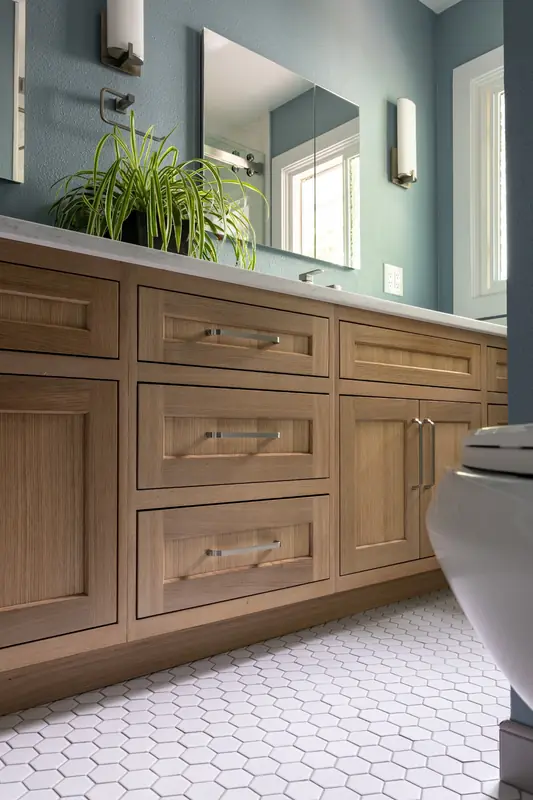 Guest bath with soft blue walls, a warm wood vanity with quartz top, a wide mirror and white hexagon tile floor