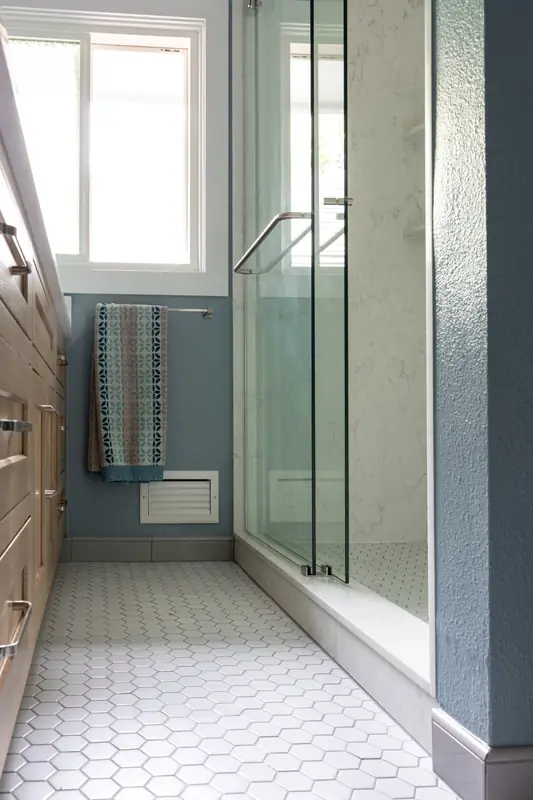 Shower glass and marble-look walls alongside the vanity and window