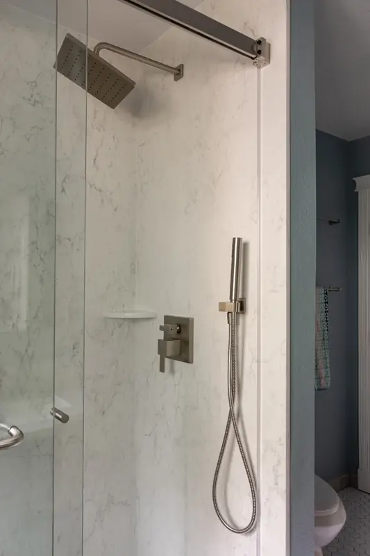 Shower with a square rain head, handheld wand and brushed nickel controls on marble-look walls
