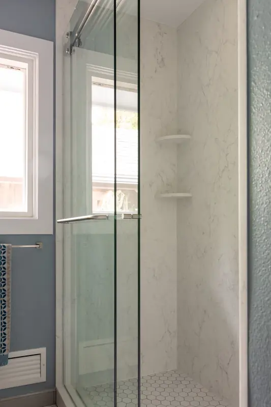 Walk-in shower behind clear glass, with corner shelves and a window for natural light