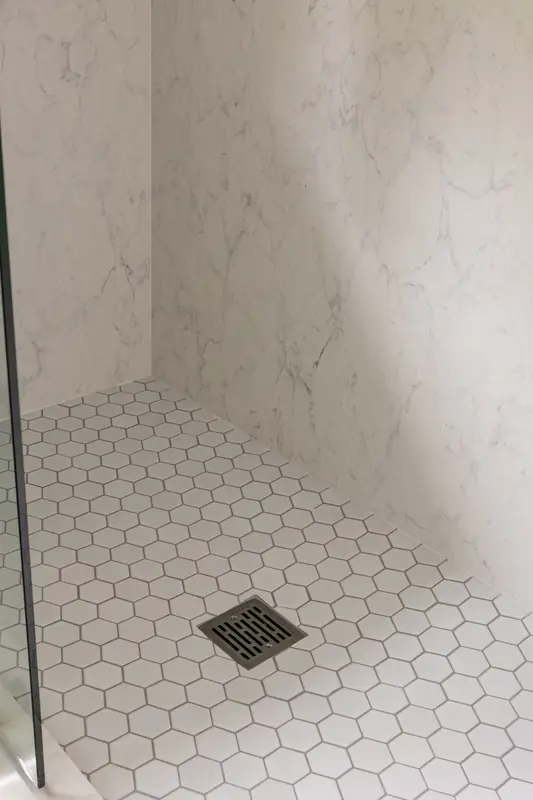 White hexagon tile shower floor with a square drain set against marble-look walls