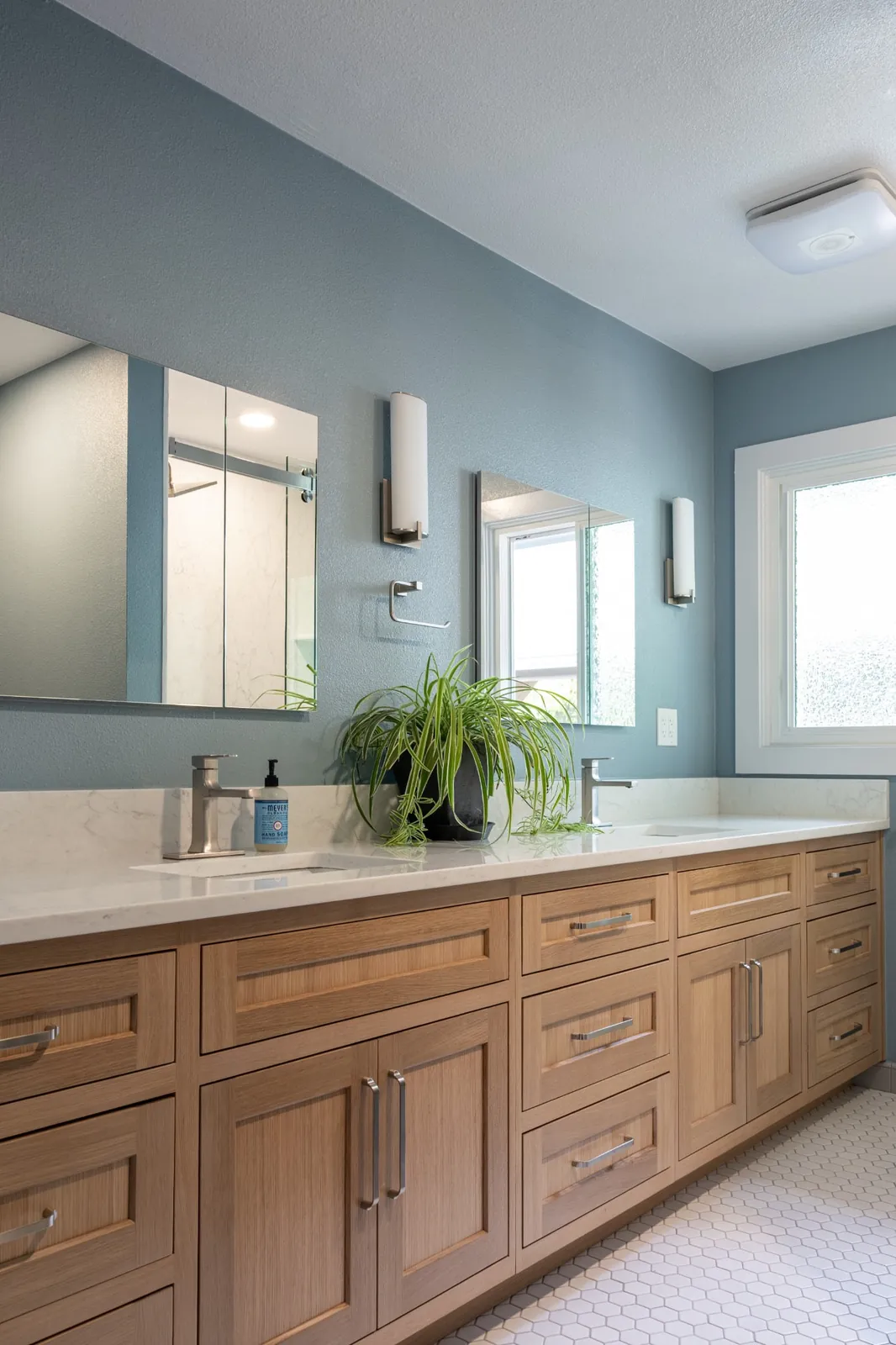 The same bathroom after remodeling: one long custom stained wood double vanity with a quartz top running where the partition wall used to stand