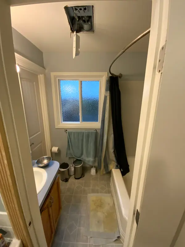 Before the remodel: the hallway half of the Jack-and-Jill bathroom with a small vanity, vinyl floor and alcove tub under the window