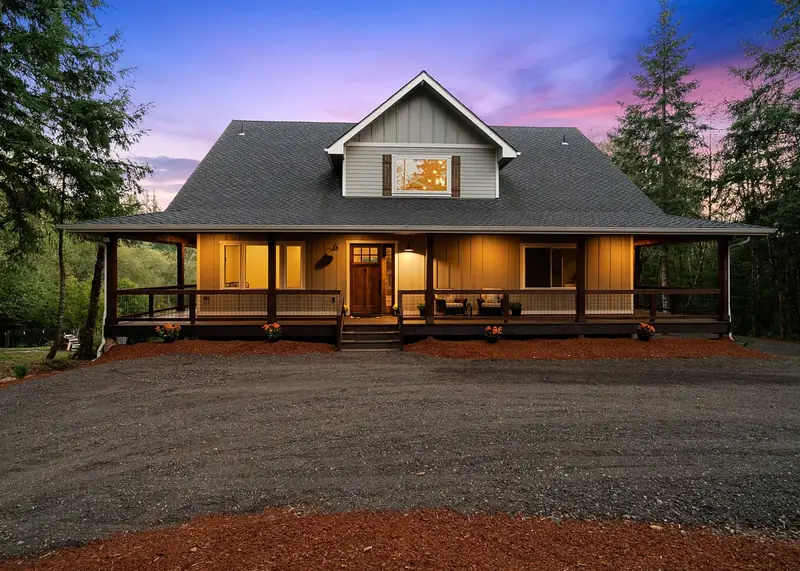 Country farmhouse with a full wraparound porch and gabled dormer lit at dusk — Country Farmhouse Build with Craftsman Influences in Battle Ground, WA