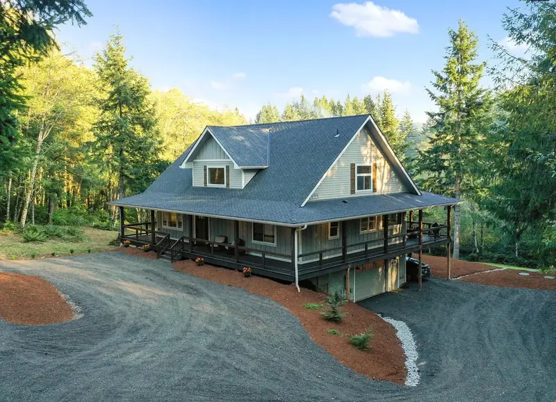 Three-quarter aerial view of the finished farmhouse on its wooded acreage — Battle Ground, WA