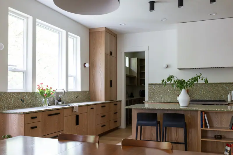 The sink wall and its bank of tall windows, with the oak island, the plaster hood and the walk-in pantry doorway beyond