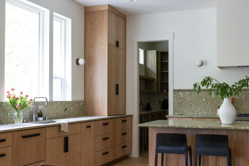 Tulips on the terrazzo-look quartz counter beside the undermount sink, with a black faucet, oak drawer banks and the pantry doorway in the background