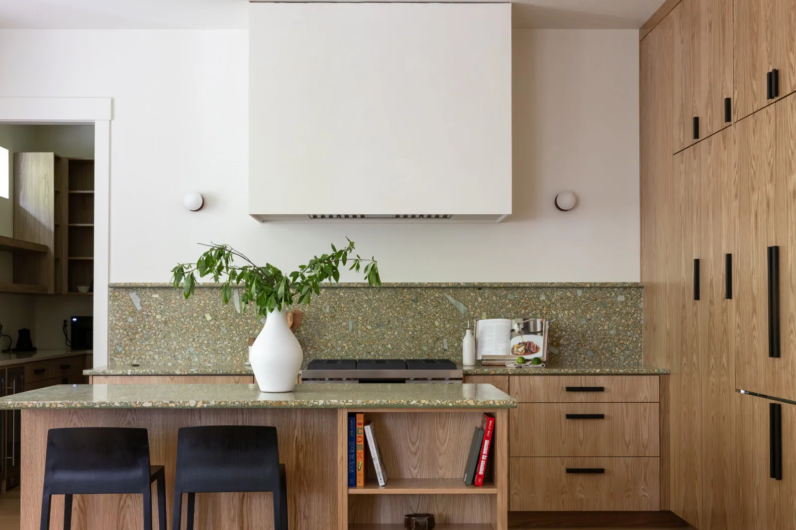 The same cooking wall after remodeling, with a plaster hood finished like the wall, terrazzo-look quartz counters and a full-height backsplash in the same stone