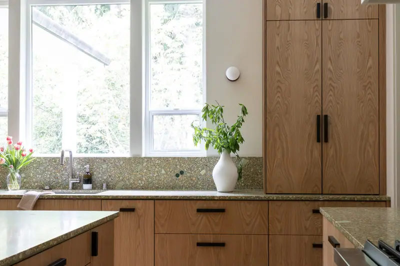 The window over the sink with the stainless range beyond and panel-clad oak appliance columns at the right