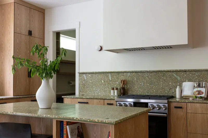 The green terrazzo-look quartz island top, the plaster hood behind it and the range wall beyond