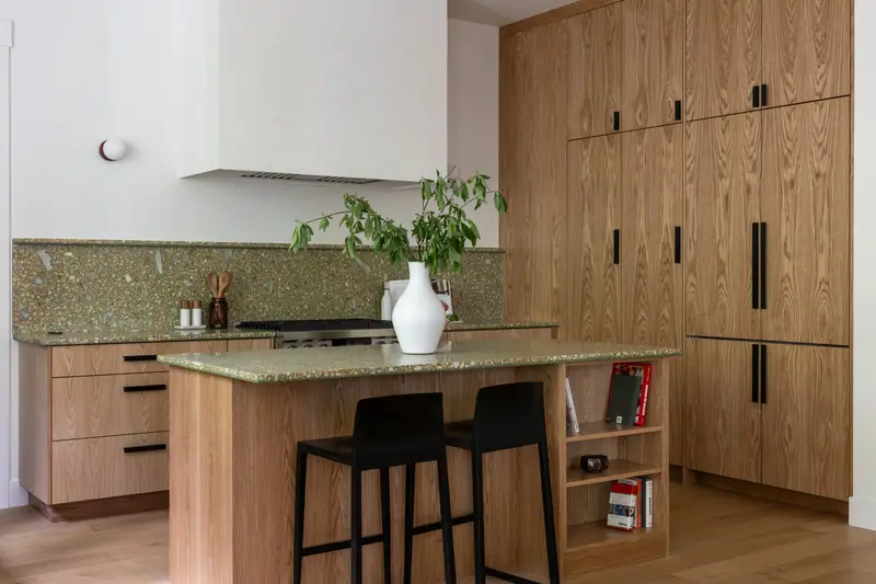 The long white oak cabinet wall alongside the island, with the range, the quartz backsplash and wide-plank oak floors