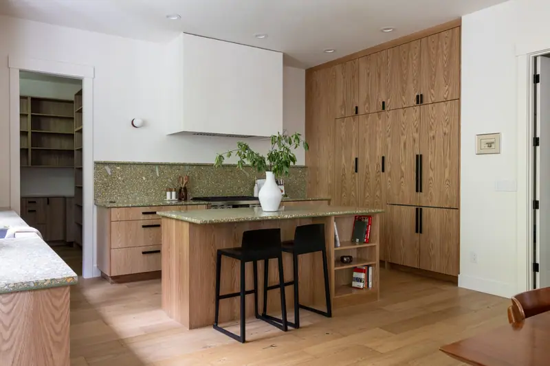The full width of the kitchen, with the walk-in pantry doorway, the plaster hood, the island and the tall oak cabinetry