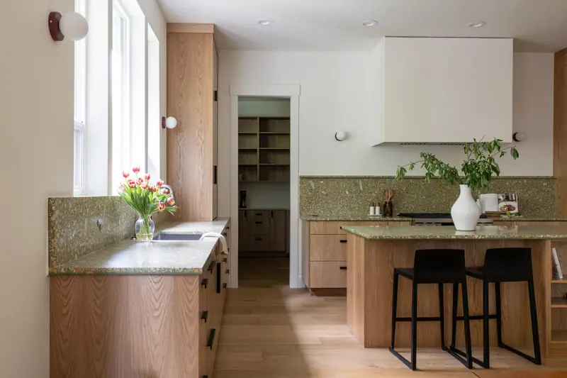 Looking across the sink counter to the pantry doorway, with the island, its black stools and the plaster hood beyond