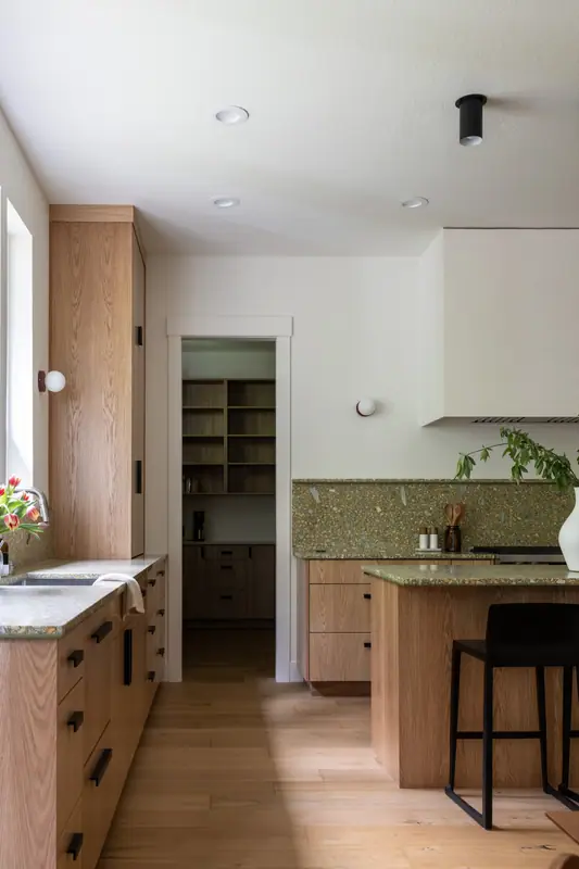 The end of the island and the pantry doorway, with oak open shelving inside the pantry and wide-plank oak floors