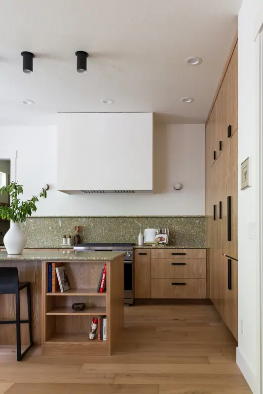 The plaster hood and full-height quartz backsplash above the range, with cookbooks in the open oak shelf at the end of the island