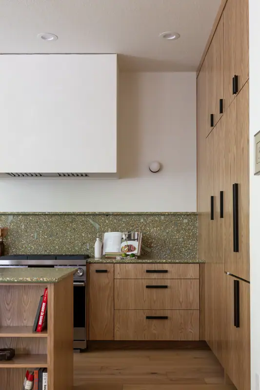 The built-in oven set into oak cabinetry beside the range, under the plaster hood and the full-height quartz backsplash