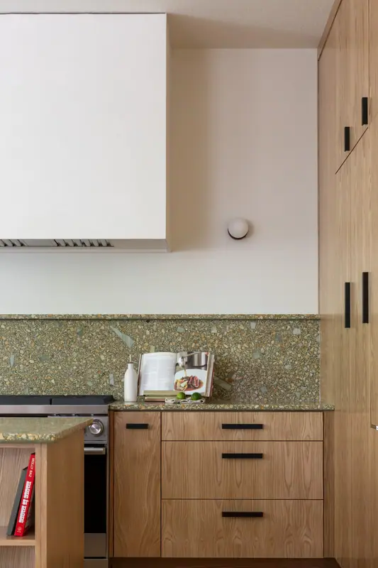 The oven, drawer bank and long matte black bar pulls of the range wall, with the quartz backsplash running to the underside of the cabinets