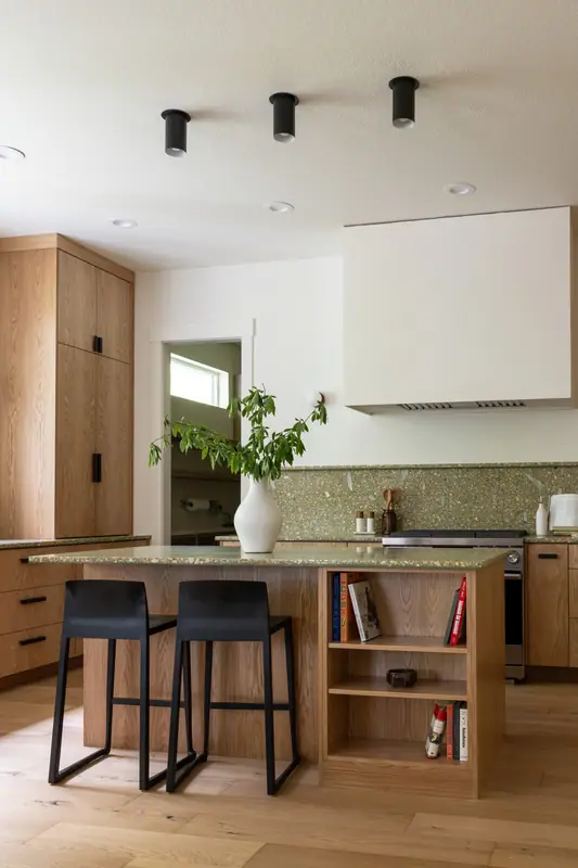 The island with two black stools and its open bookshelf end, with the plaster hood and the tall oak cabinet run behind
