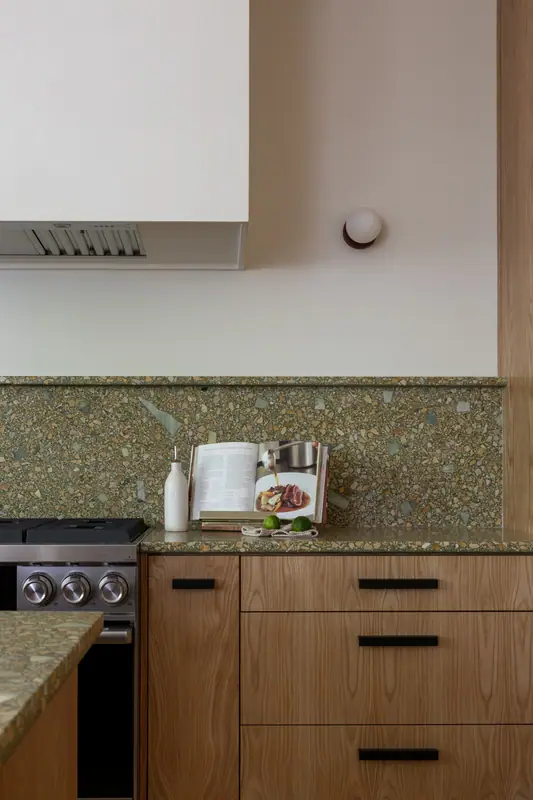 The stainless range with its knobs and the quartz backsplash rising behind it, under the plaster hood