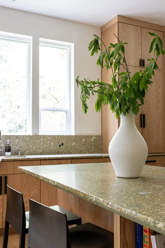 The quartz island top and a tall oak cabinet at the window end of the kitchen
