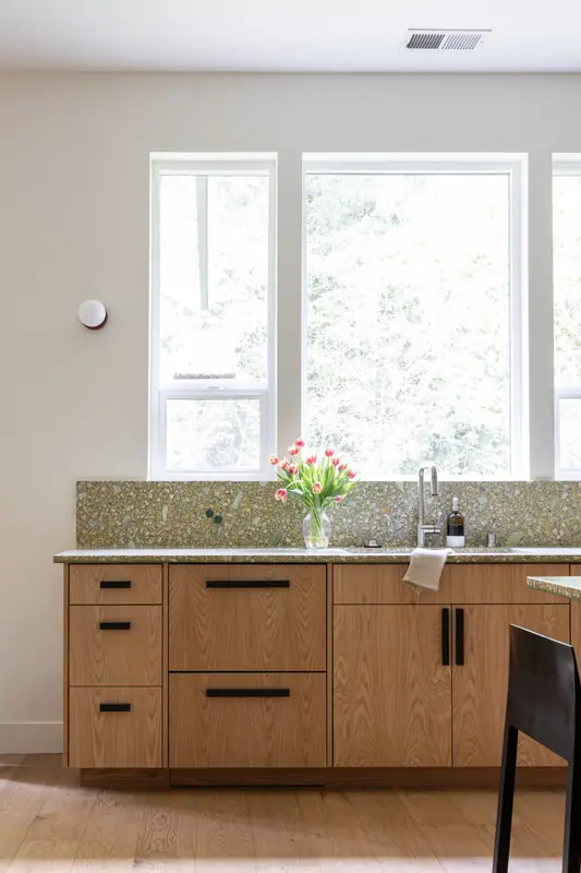 The sink wall in detail: tall windows, undermount sink, black faucet and white oak base cabinets with long black pulls