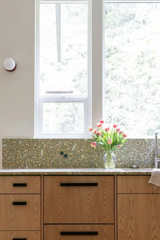 Tulips at the window above the sink, with the quartz backsplash and oak drawer banks with matte black bar pulls