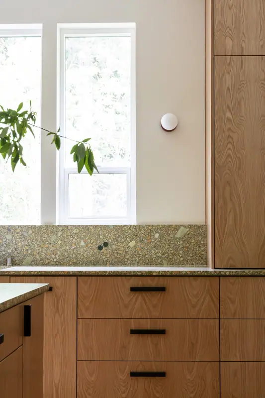 The window end of the counter run, with the tall oak cabinet, the quartz backsplash and a drawer bank below