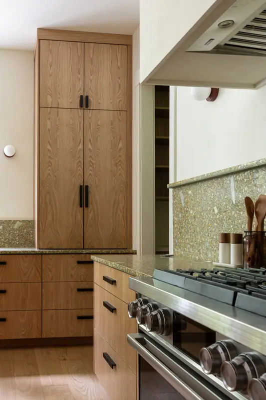 The stainless gas cooktop and the hood liner above it, with a utensil crock, the quartz backsplash and the pantry doorway beyond