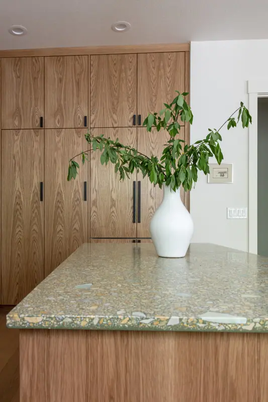 The quartz island top and vase against the wall of full-height white oak cabinetry, with outlets set into the stone