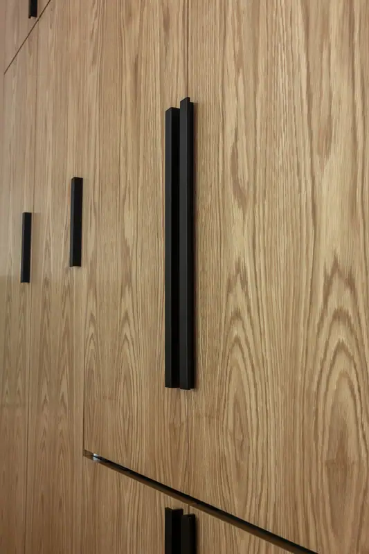 Grain detail of the plain-sliced white oak fronts and the long matte black bar pulls that open them