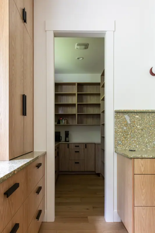 The open pantry doorway showing custom oak shelving inside, with the kitchen counter at the right