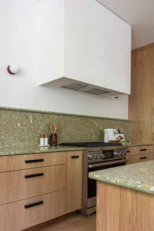 The cooking wall: plaster hood with a stainless liner, full-height quartz backsplash, stainless range and oak drawer banks