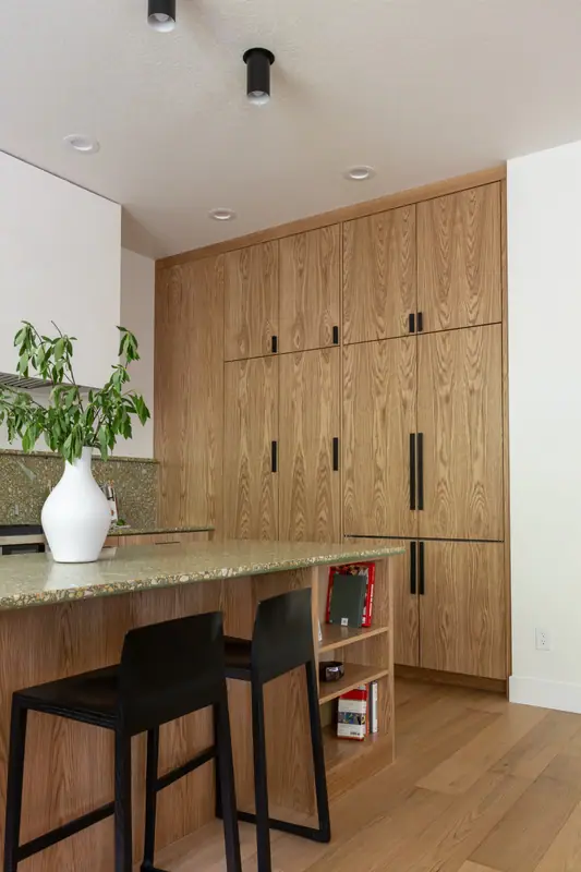 The long wall of full-height white oak cabinetry, with the island, its black stools and the quartz counters