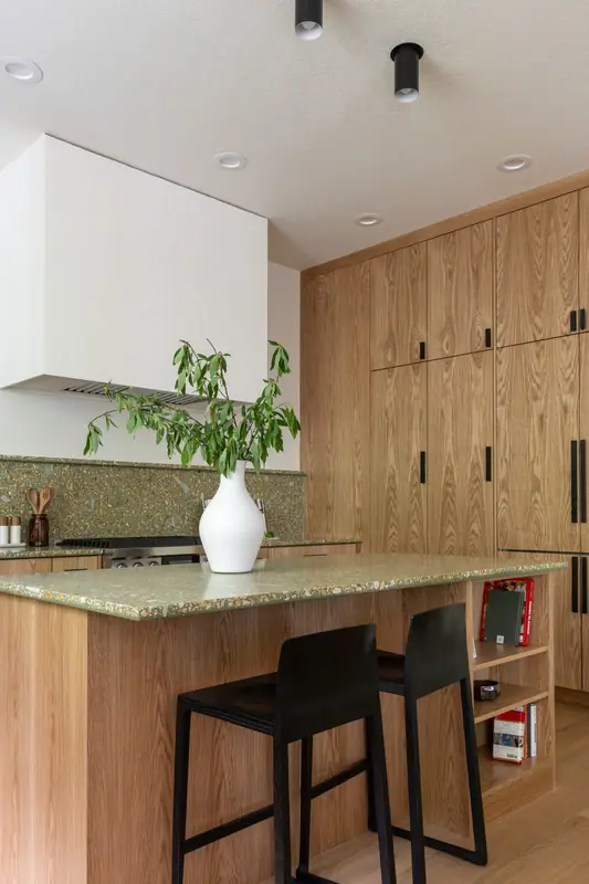The plaster hood, the tall oak cabinet run and the island with two black stools and cookbooks