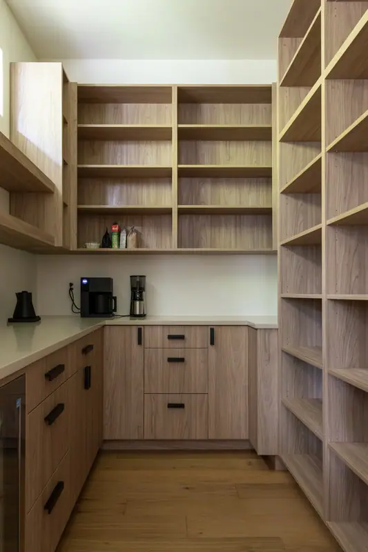 The walk-in pantry with oak open shelving on two walls, base cabinets and a counter holding the coffee maker