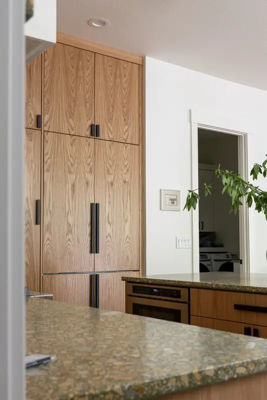 The appliance wall in full: oak-panelled refrigerator doors, a built-in oven and warming drawer, and the island counter in the foreground