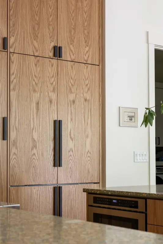 Close detail of the refrigerator hidden behind full-height white oak panels, with the long matte black bar pulls that open them