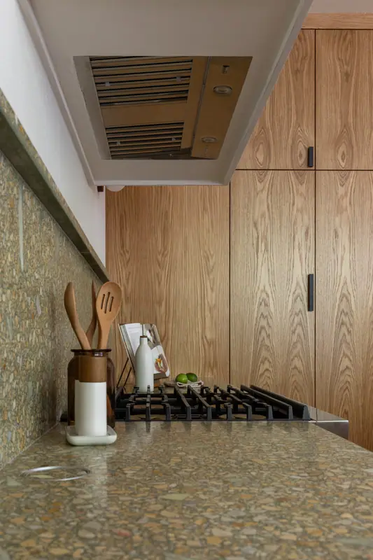 The stainless gas cooktop set into the terrazzo-look quartz counter, with the hood liner above and the quartz backsplash behind
